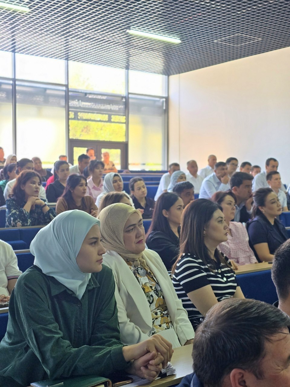 Audience of people seated in tiered lecture hall, attentively watching a presentation